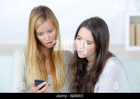 Due orinato giovani donne guardando al telefono cellulare Foto Stock