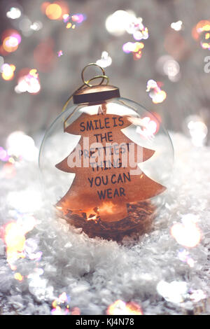 Natale e Anno nuovo sfondo - sfera di vetro con citazione "un sorriso è la più bella cosa che si può indossare', una candela e le luci di Natale sul tavolo di legno Foto Stock