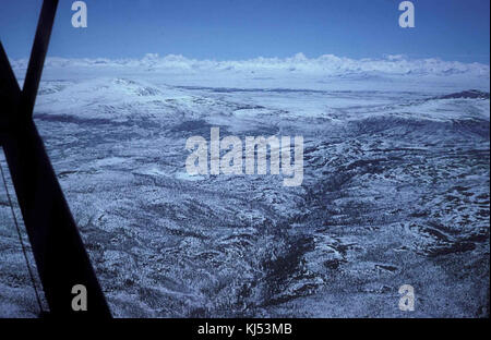 Uno scatto aereo di una regione montuosa durante l'inverno, che mostra vette innevate e terreni accidentati, con la neve che ricopre il paesaggio sottostante. Foto Stock