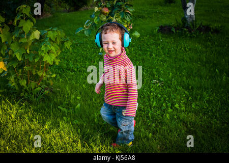 Funny toddler boy canta a sintonizzare le cuffie a piedi un prato al tramonto Foto Stock