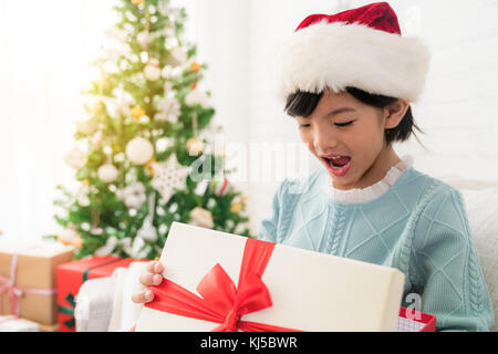 Close up poco carino ragazza asiatica apre la sua bocca e sentirsi sorpreso faccia espressione dopo lei si apre il regalo di Natale scatola seduta un divano nel de Foto Stock