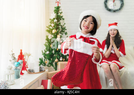 Grazioso piccolo ragazzo asiatico tenendo una calza di Natale chiedendo per il regalo di Natale da Santa di fronte alla telecamera in vacanza invernale stagione. Foto Stock