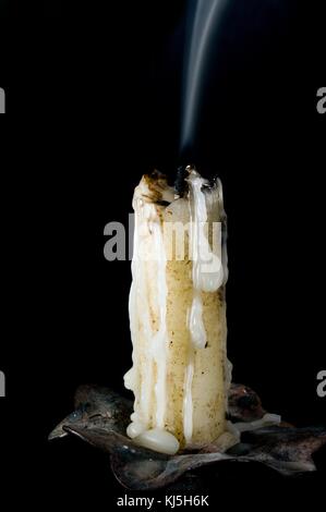 Candela appena spenta con il fumo e la cera fusa di cadere in un lampadario isolato in nero Foto Stock