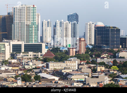 Vista aerea di un basso edificio residenziale in contrasto con un moderno condominio e torri di uffici nel cuore di Jakarta, Indonesia città capitale. Foto Stock