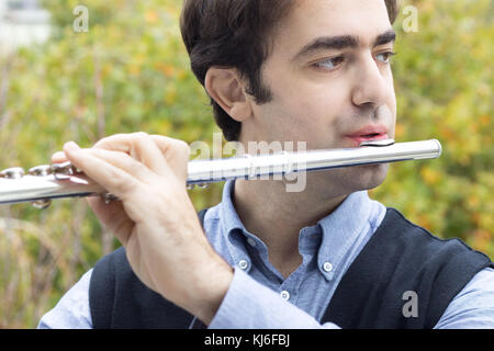Un maschio flautista giocando a Silver flauto traverso all'aperto, vista di profilo, primo piano. Foto Stock
