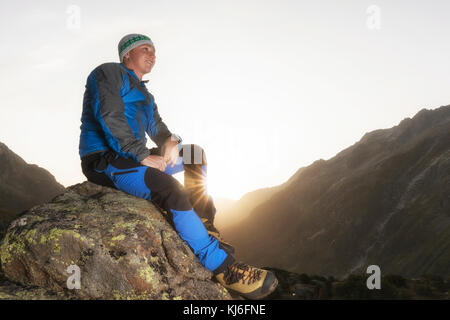 Bella giovane escursionista prendendo una pausa su una pietra e gode il sunrise nelle montagne svizzere Foto Stock