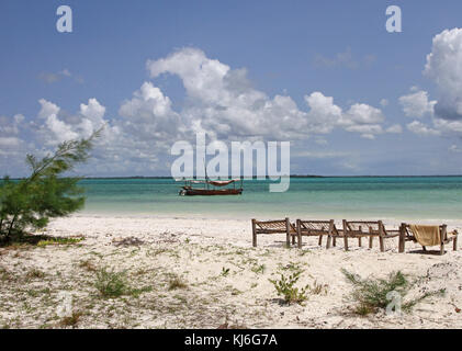 Dhow nell'oceano e lettini in legno sulla spiaggia, Zanzibar, isola di Unguja, Tanzania. Foto Stock