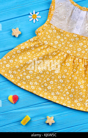 Baby-girl giallo sundress. cotone abiti estivi in piccoli fiori bianchi per bambine blu su sfondo di legno. bella decorazione da caramelle di gomma Foto Stock