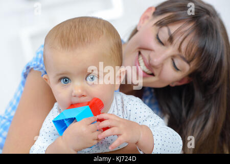 Madre sorridente al bambino giocattolo da masticare Foto Stock