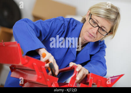 Medio-età della donna in tute le riparazioni facendo con il suo strumento-box Foto Stock