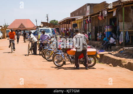 Diversi boda boda moto taxi schierate parcheggiato su una strada polverosa con persone camminare in una città, Busia, Uganda, Africa orientale Foto Stock