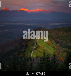 Jamnik, Slovenia - veduta aerea del bel tramonto dorato alla chiesa di San Primoz di Jamnik. Alpi Giulie alla luce del sole Foto Stock