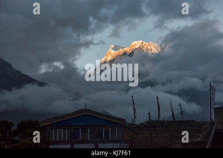 Annapurna iii visto attraverso le nuvole di sunrise, con ngawal borgo sottostante, circuito di Annapurna, Nepal Foto Stock