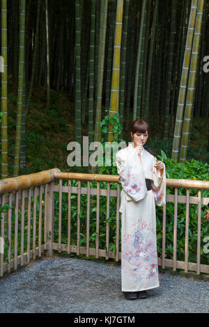 Giapponese giovane donna in kimono, di fronte a una foresta di bamboo a Kyoto, Giappone Foto Stock