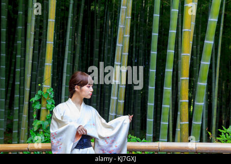 Giapponese giovane donna in kimono, di fronte a una foresta di bamboo a Kyoto, Giappone Foto Stock