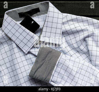 Uomini bianchi a scacchi strippato Dress shirt, nuovo di zecca, con le etichette sulla parte superiore di colore nero di superficie in legno Foto Stock