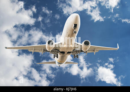 Bassa volare aerei civili con atterraggio contro il blu cielo nuvoloso, vista dal basso Foto Stock