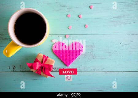 Valentines colazione con un giallo la tazza di caffè, rosa Cuore in plastica, poco presenti, caramelle rosa e di amore è il testo scritto in nastro su un turchese wo Foto Stock