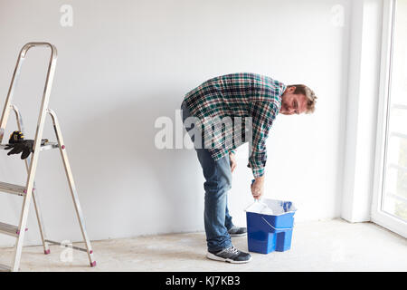 Giovane pittura un muro su bianco in una casa moderna Foto Stock