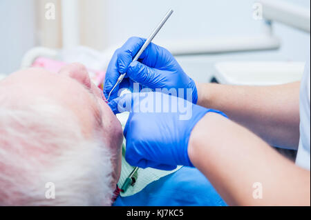 Close up dentista mani guanti nel trattare un paziente anziano in stomatologia moderna clinica. messa a fuoco selettiva. spazio per il testo vista posteriore. Foto Stock