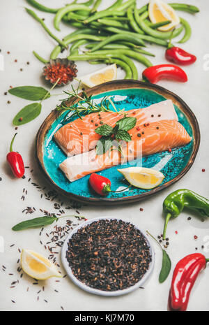 Crudo di pesce Salmone bistecche di filetto con verdure, verdi, riso, spezie e limone in blu luminoso su piastra di marmo grigio Sfondo. Pulire mangiare, dieta, Foto Stock