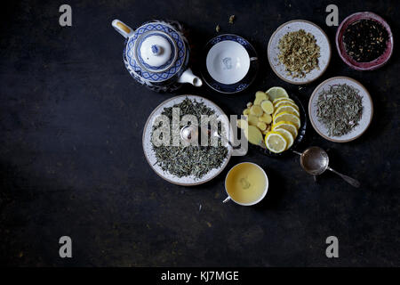 Foglie di tè diverse con fette di limone su sfondo scuro Foto Stock