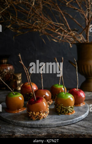 Vassoio di marmo pieno di caramello le mele con stick gestisce coperto di noci e semi. Moody caduta delle foglie in background. Foto Stock