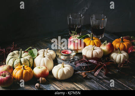 Autunno decorazione tabella vacanza con zucche decorative, mele, foglie rosse, bicchieri di vino rosso, candela su tavola di legno. Stile rustico Foto Stock