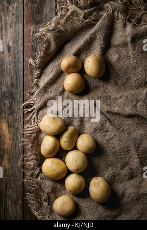 Crudo Intero organico lavato le patate su un letto di sacco su un vecchio ceppo di legno dello sfondo. Vista da sopra con uno spazio