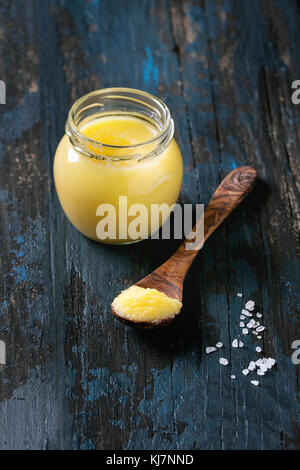 Bicchiere di acqua salata aspirata ghee burro in piedi con il cucchiaio di legno e sale marino su un vecchio blu scuro dello sfondo di legno. Mangiare sano. Foto Stock