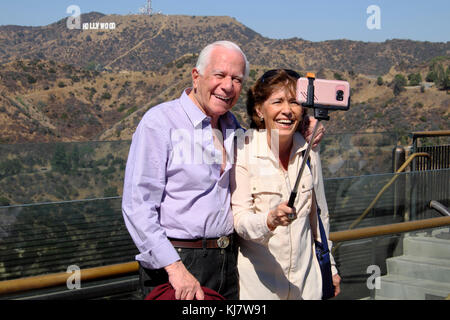 Coppia senior con selfie stick senior ridendo con la fotocamera del telefono cellulare e segno di Hollywood Griffith Park Observatory Los Angeles LA USA KATHY DEWITT Foto Stock