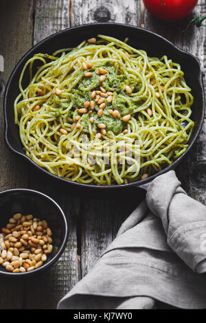 Close-up di italiano spaghetti con il pesto e pinoli in nero ghisa padella sulla tavola in legno rustico. Foto Stock