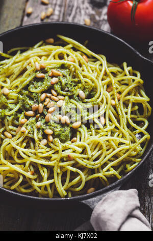 Close-up di italiano spaghetti con il pesto e pinoli in nero ghisa padella sulla tavola in legno rustico. Foto Stock