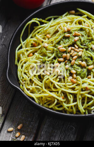 Close-up di italiano spaghetti con il pesto e pinoli in nero ghisa padella sulla tavola in legno rustico. Foto Stock