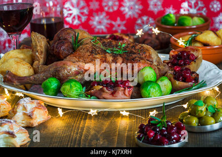 Festive anatra arrosto su un tavolo di legno con i cavoletti di Bruxelles, patate al forno, mele e salsa di mirtilli sul tavolo di legno Foto Stock