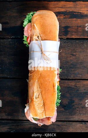 Sottomarino lungo sandwich con prosciutto e verdure su sfondo di legno dal di sopra Foto Stock