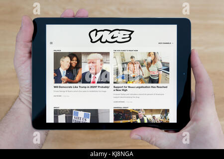 Un uomo guarda il Vice sito sul suo iPad dispositivo tablet, sparato contro un tavolo di legno top sfondo (solo uso editoriale) Foto Stock