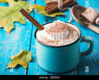 Pumpkin spice latte con panna montata e cannella in tazza rustico su sfondo blu Foto Stock