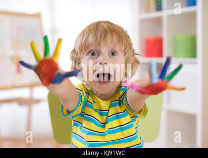 Ragazzo bambino disegna con le mani e mostra multi-verniciato colorato palms. bambini giochi educativi con vernici. Foto Stock