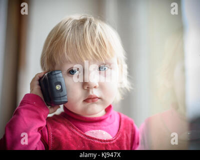 Piccola ragazza in un abito rosso parlando al telefono Foto Stock