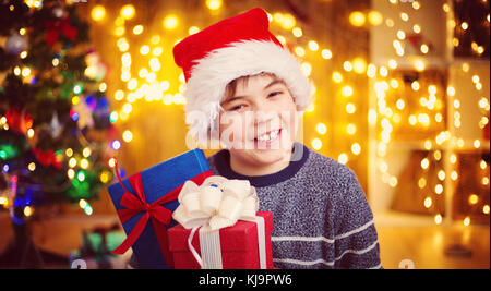 Ragazzo seduto sul pavimento con presenta vicino albero di natale Foto Stock