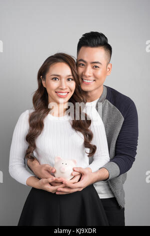 Coppia giovane tenere maiale rosa in piedi su sfondo grigio Foto Stock