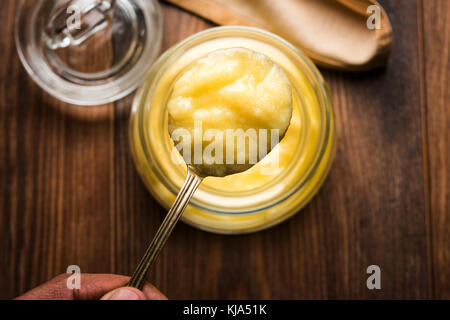 Desi ghee o burro chiarificato in vetro o rame contenitore o barattolo in ceramica con cucchiaio, il fuoco selettivo Foto Stock