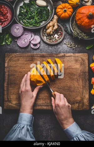 Donna femmina mani tagliare la zucca sul tagliere con coltello e varie verdure e condimenti per il gustoso piatto stagionale per la cottura, rustico Foto Stock