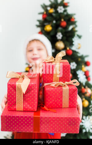 Ritratto di carino divertente bambino vestito di rosso notte pigiami e hat di santa. sfocata white capretto felice azienda pila di vacanza presenta in mani e Foto Stock