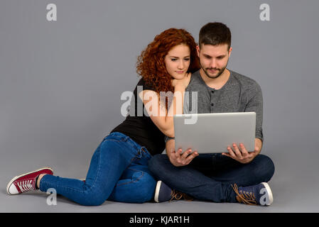 Una bella coppia giovane seduto per terra e che guardano un notebook e sorridente Foto Stock