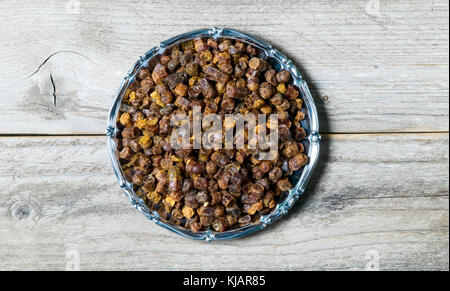 Granuli di propoli all'interno della piastra su sfondo di legno, prodotti apistici Foto Stock