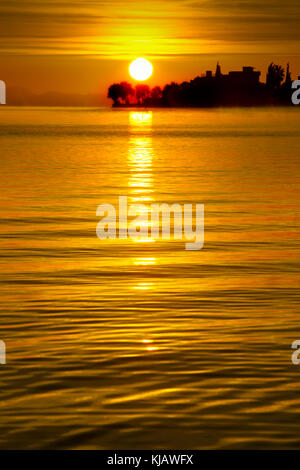 Il sole sorge sopra l'orizzonte e viene riflessa dalle dolci increspature del mare. Foto Stock