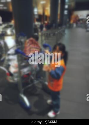 Sfocate, al di fuori della messa a fuoco e bokeh foto di una bambina in attesa con il trolley in un aeroporto. Foto Stock