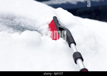 Nevoso inverno in una città in una giornata di sole. auto dopo la nevicata nel parcheggio. giovane donna cercando di aprire il gelido auto . Foto Stock